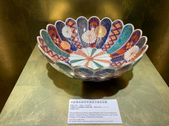写真：美しく絵付けされた菊花をかたどった鉢が展示されている様子。「色絵菊花唐花花菱雲紋菊花形鉢」の作品名札がついている
