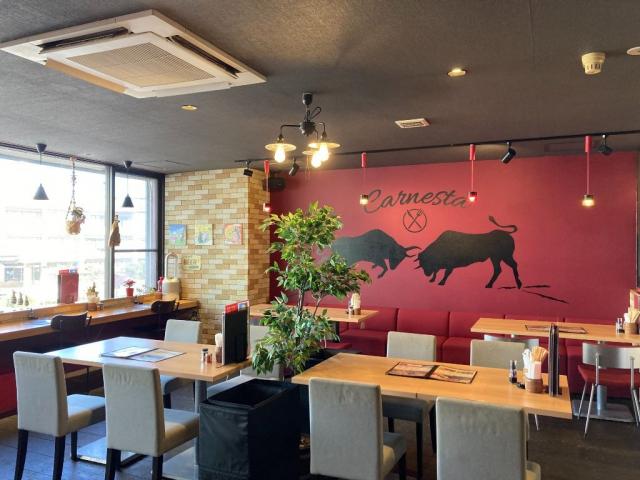写真：『唐津 孤高の肉バル カルネスタ』の店内。テーブル席の奥の赤い壁面に、スペインをイメージさせる牛のシルエットが描かれている
