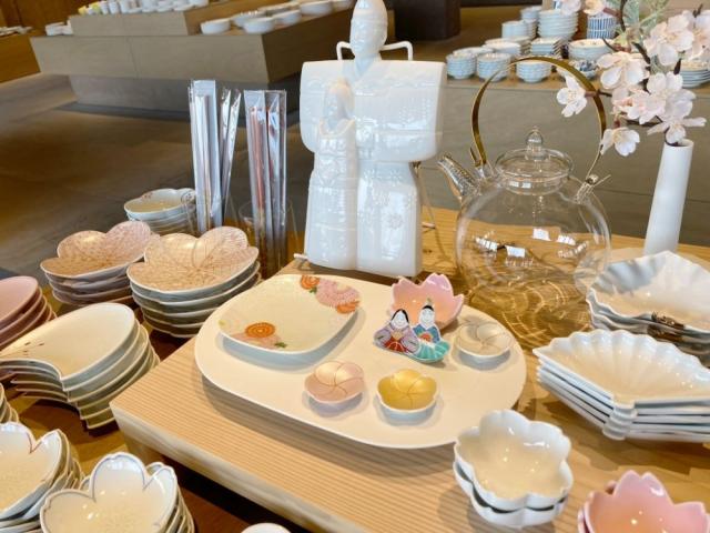 写真：梅形・桜形・扇形などの小皿の売り場に桜の造花ややきもの雛人形がディスプレイされている様子