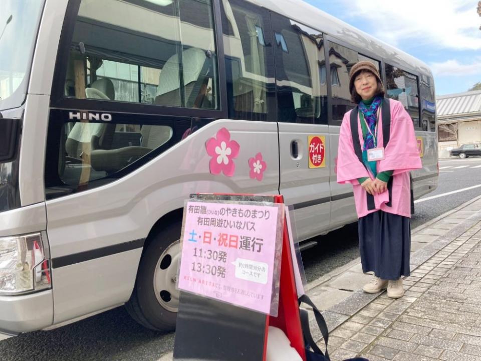 写真：周遊バスの立て看板と、停車している周遊バスの前に立つ女性ガイド