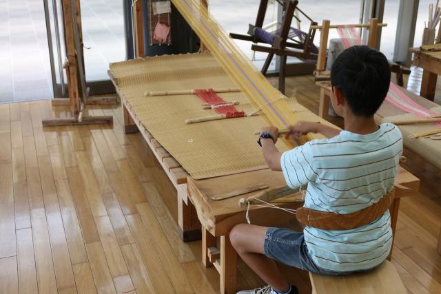 写真：古代の道具を使って布織りづくりする少年