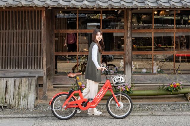 写真：旧牛島家の前でチャリチャリの赤い自転車を押している笑顔の女性