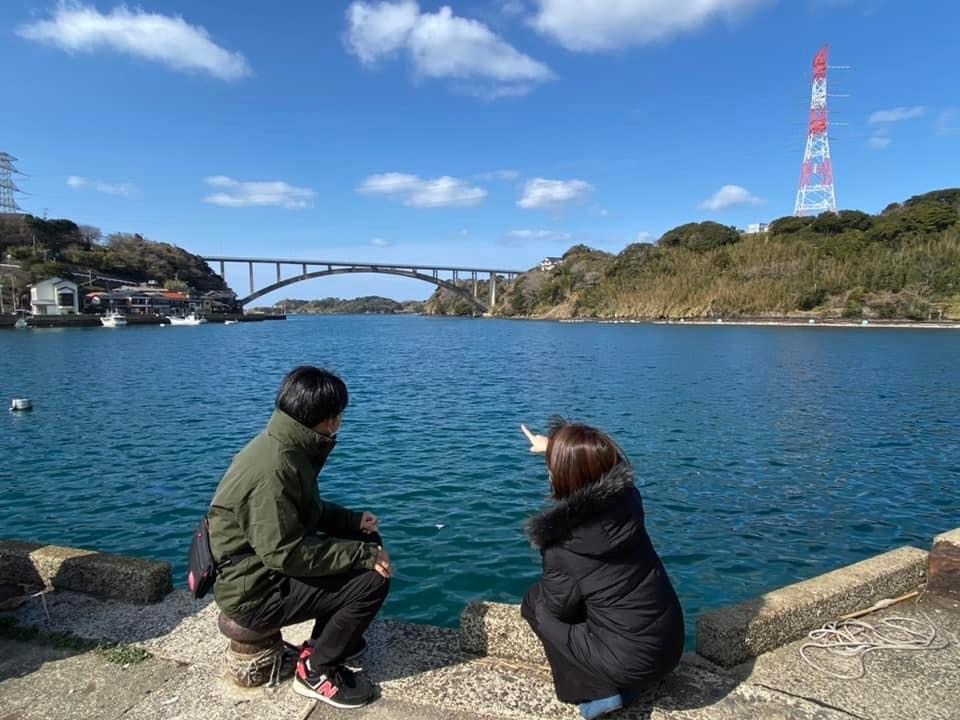 写真：男女2名が海辺で遠くの橋を眺めている様子