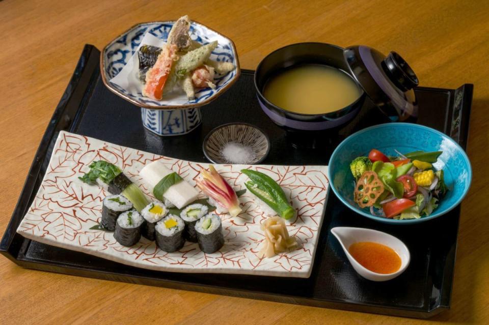 写真：手前に野菜の巻き寿司と握り寿司が盛られた皿、右に野菜サラダ、奥の右に野菜の天ぷら、奥の左にみそ汁があるセット料理