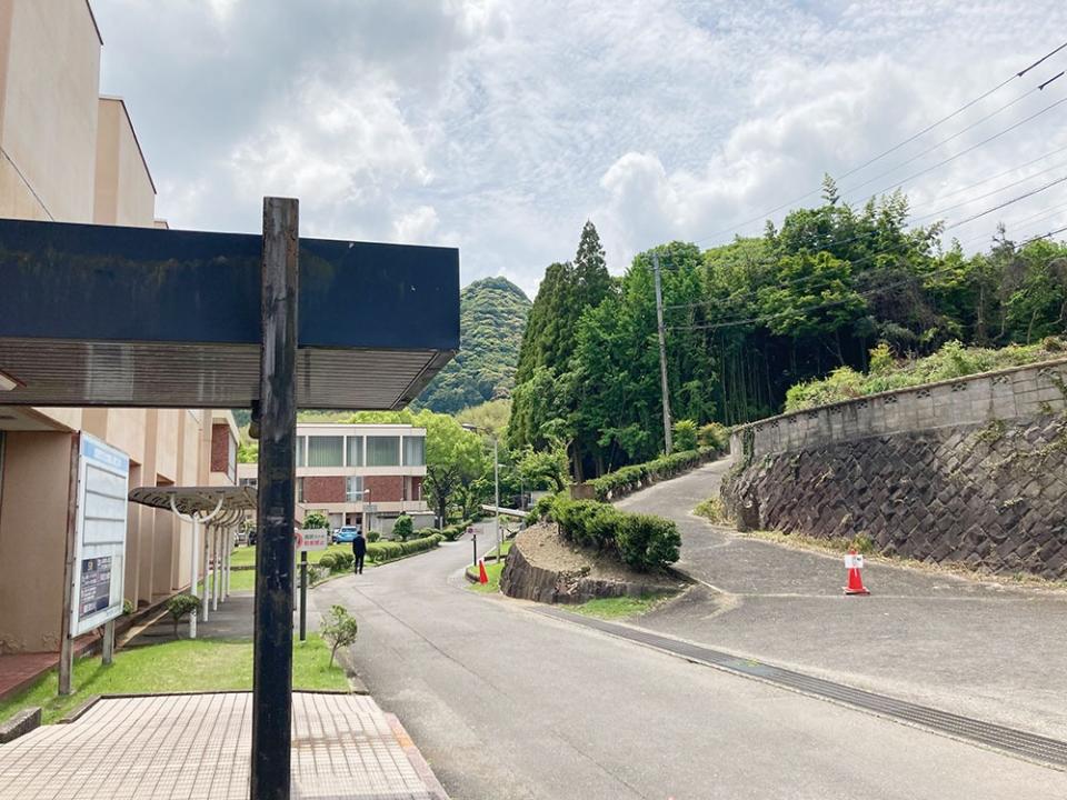 写真：左側に武雄市文化会館の建物入り口があり、画面中央の道を挟んで右側に坂がある風景