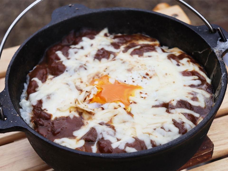 写真：鉄鍋で炊いたごはんにカレーとチーズと卵を乗せて焼いている様子