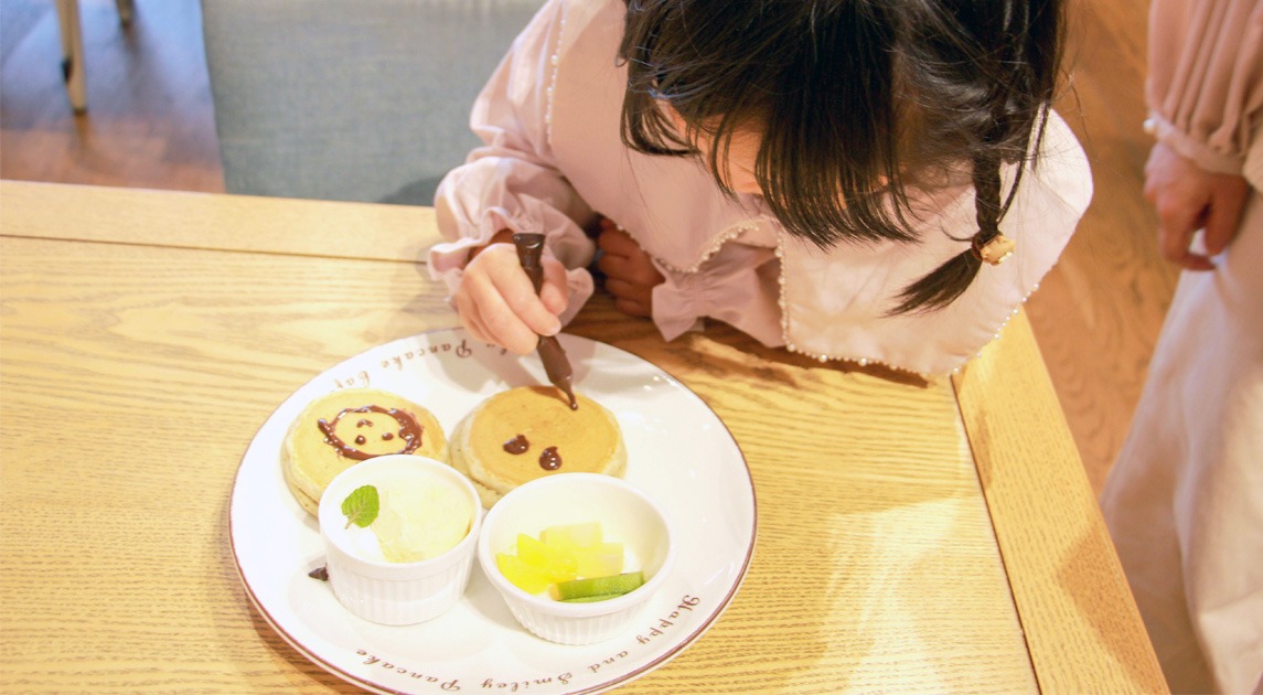写真：子供がパンケーキにチョコペンで絵を描いている様子