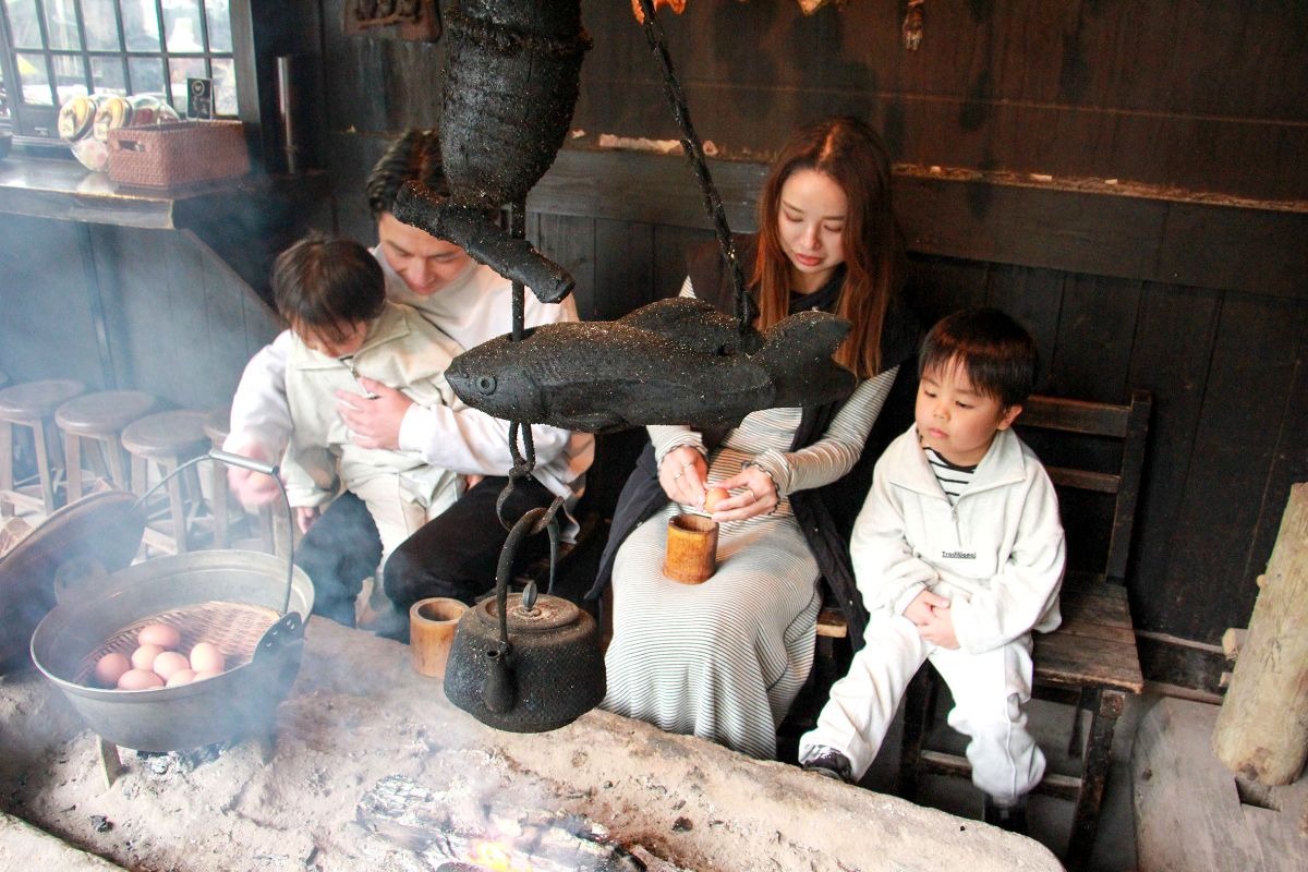 写真：蒸し場に大きな鍋がセットされており、ざるに乗せられた卵が鍋に入っている。両親と子供2人の家族が卵を見守っている