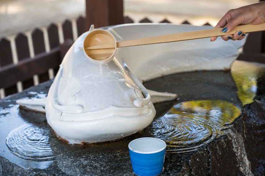 写真：白い陶器で出来た手水鉢から柄杓で水をくむ様子