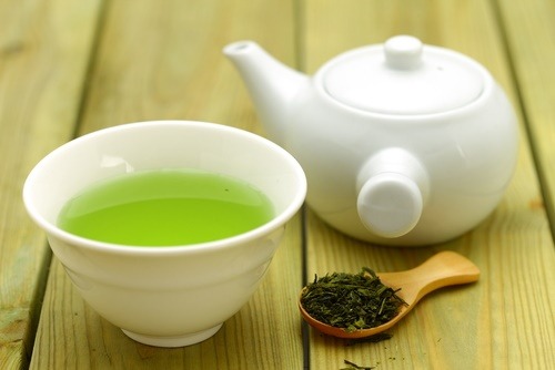 写真：緑茶の入った白い湯飲みと急須と茶葉の乗った茶匙