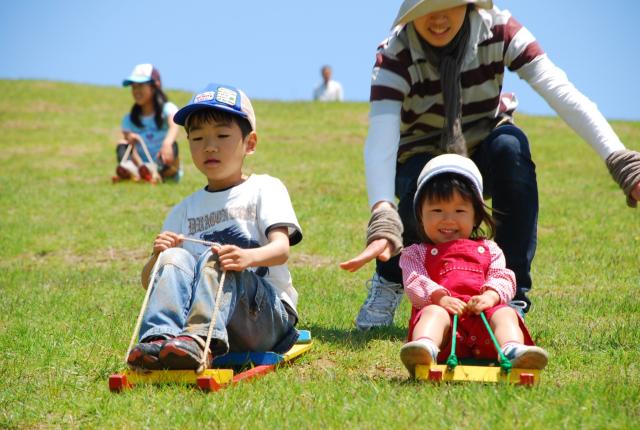 写真：草スキー場でそりを楽しむ男児と女児と母親