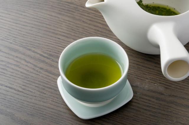 緑茶が入った青磁の湯のみと奥に白い急須がある画像