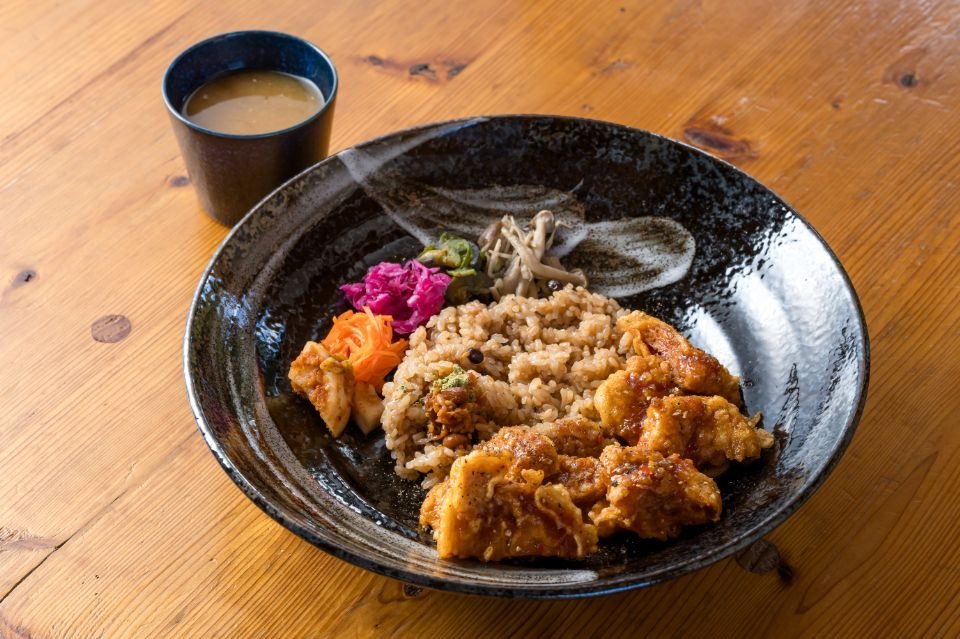 黒く丸い皿に大豆ミートのトムヤムクンとご飯、野菜キムチなどが盛られた料理画像