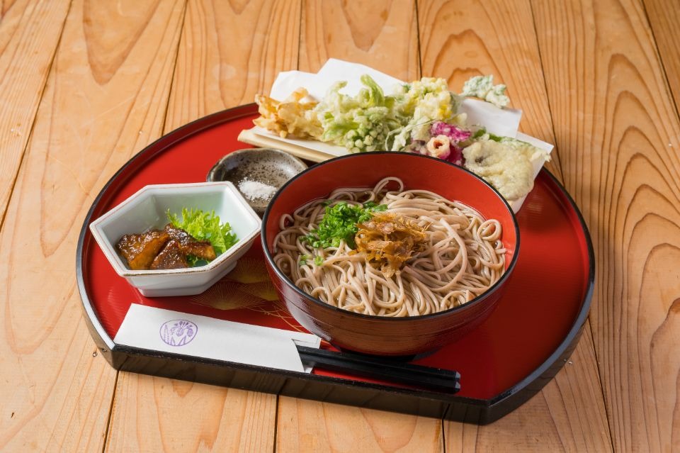 右に蕎麦、奥に野菜の天ぷら、左に小鉢がお盆の上にある料理画像