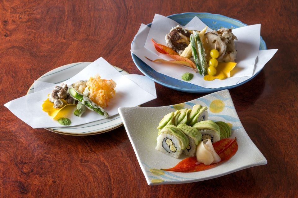 手前に白く白い皿に盛られたアボカド巻きずしと野菜の天ぷらが2皿並んだ料理画像