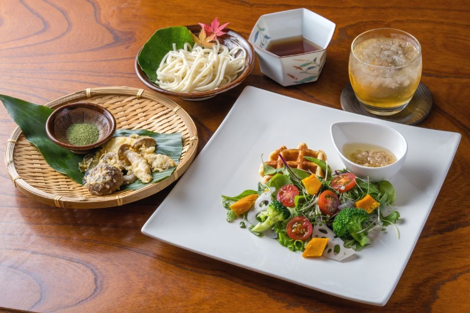 右手前にワッフルサラダ、左に野菜ときのこの天ぷら、上にうどん麺とつゆ、右奥にジュースがある画像