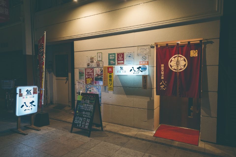 左側に八木と書かれた電飾看板があり、白い壁に赤い暖簾がかかった夜の店舗外観画像