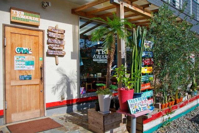 白い壁と木製のドアに、カラフルな板看板と植物が飾られた店舗外観画像
