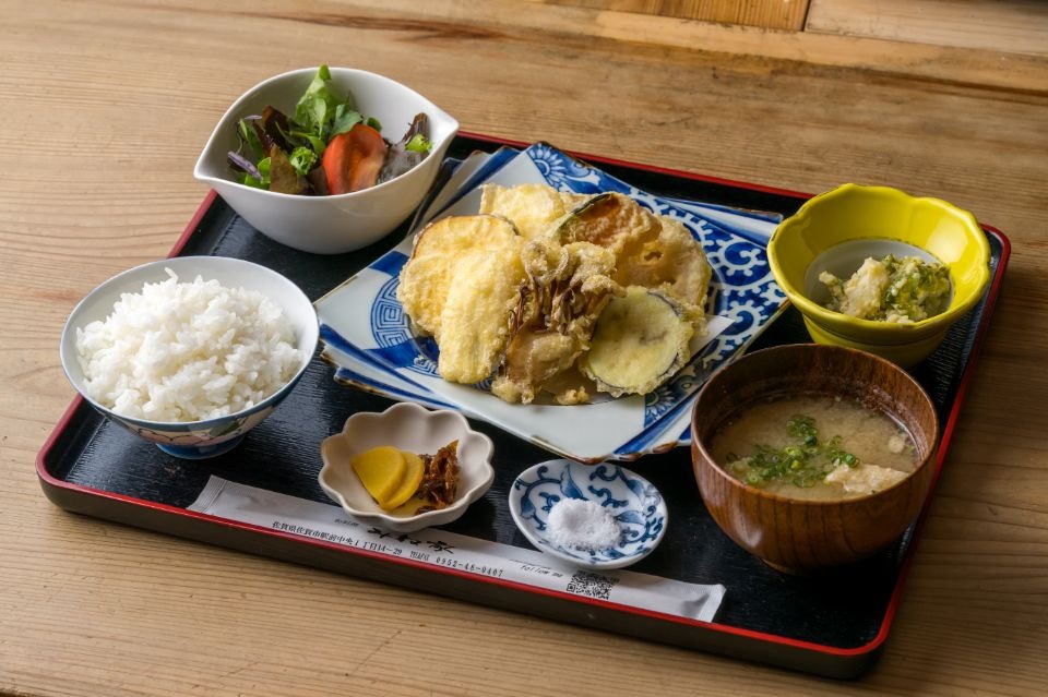 真ん中に野菜の天ぷらがあり、周りにご飯、味噌汁、サラダ、小鉢、漬物、塩があるご膳