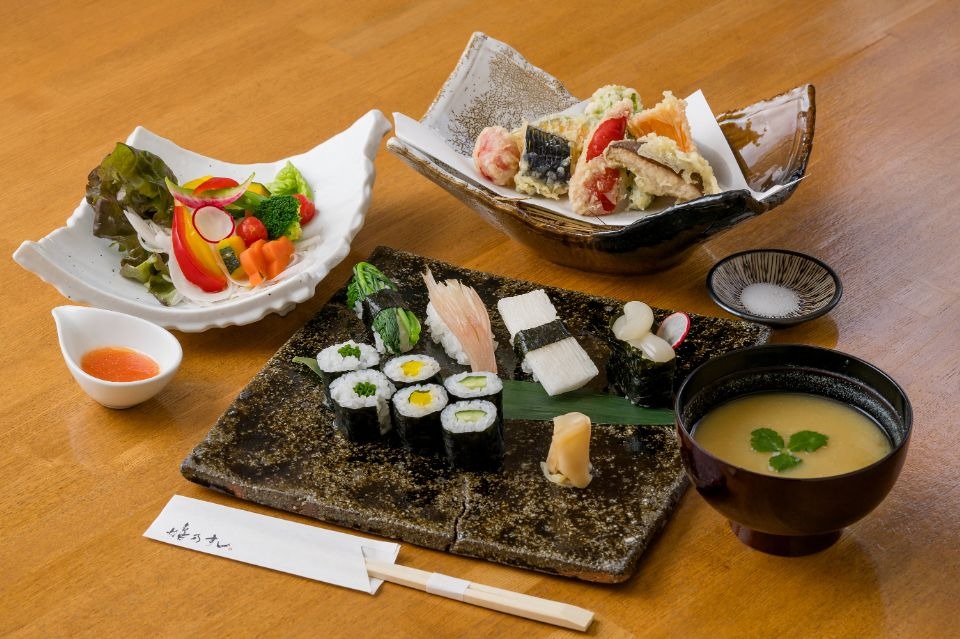 手前真ん中に野菜の寿司盛り、周りに味噌汁、野菜の天ぷら、サラダ、ドレッシングがある定食画像